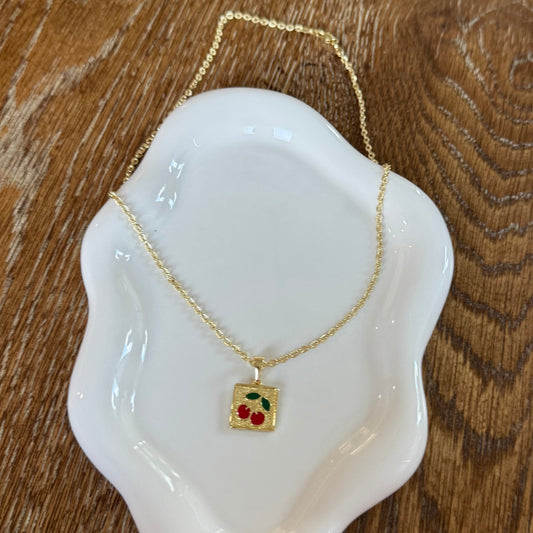This image displays the LORY NECKLACE, featuring an elegant square pendant with a golden frame, elegantly suspended from a matching gold chain. The pendant is adorned with a striking red gemstone at its center, adding a vibrant contrast.